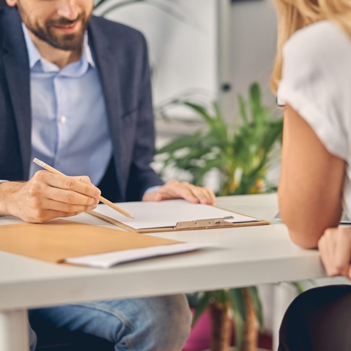 Close up of gentleman holding pencil and smiling while sitting across the table from female colleague